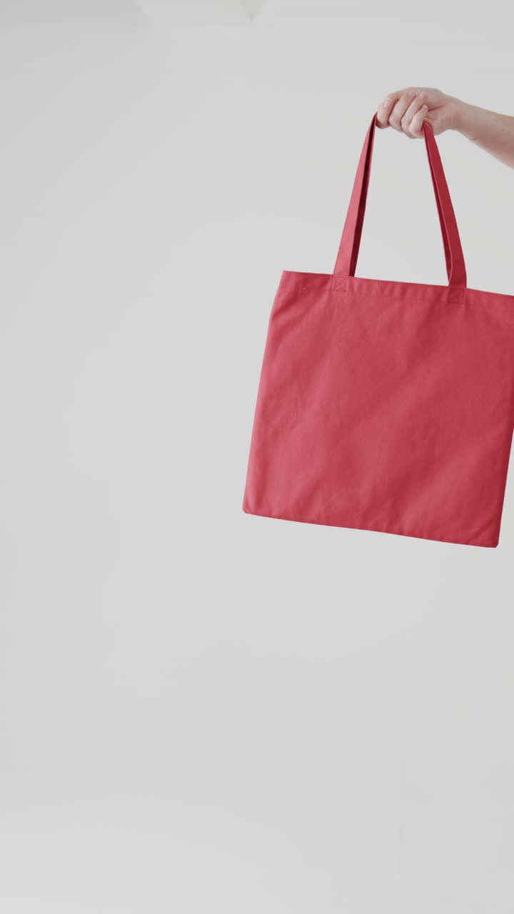 Vertical video of hand of caucasian woman with red canvas bag and copy space on white background
