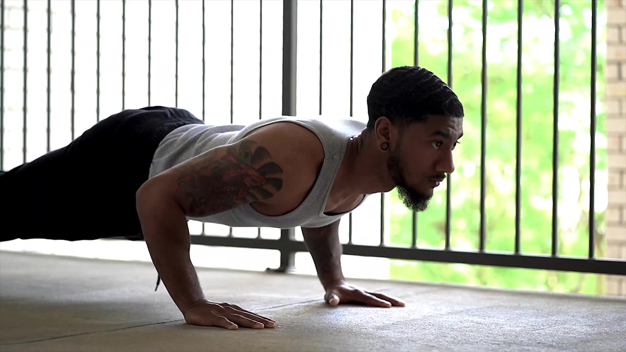 Young fit male doing pushups in slow-motion on a sunny day outdoors.