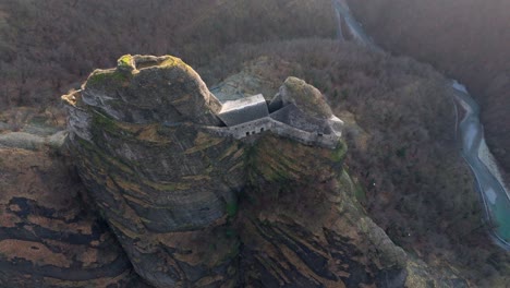 ancient castle atop a rugged cliff with a river winding in the background at dusk, aerial view