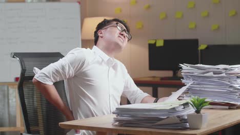 asian man having backache while working hard with documents at the office