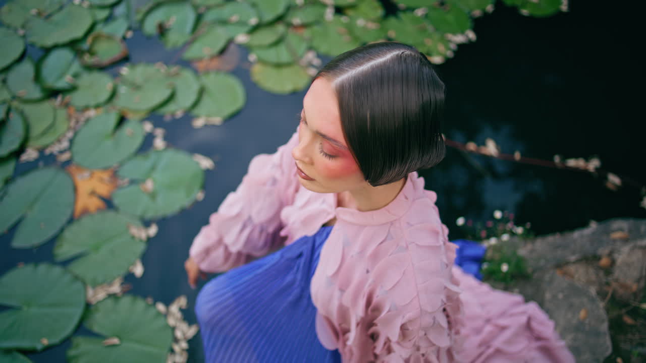 물 요정이 자연 연못에 앉아 신비한 시선을 가진 카메라를 보고 있습니다.