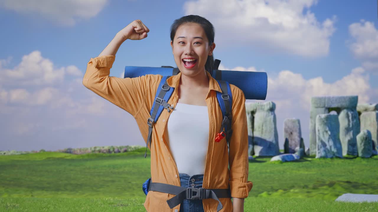 Asian Female Hiker With Mountaineering Backpack Smiling And Flexing Her Bicep While Traveling In Stonehenge