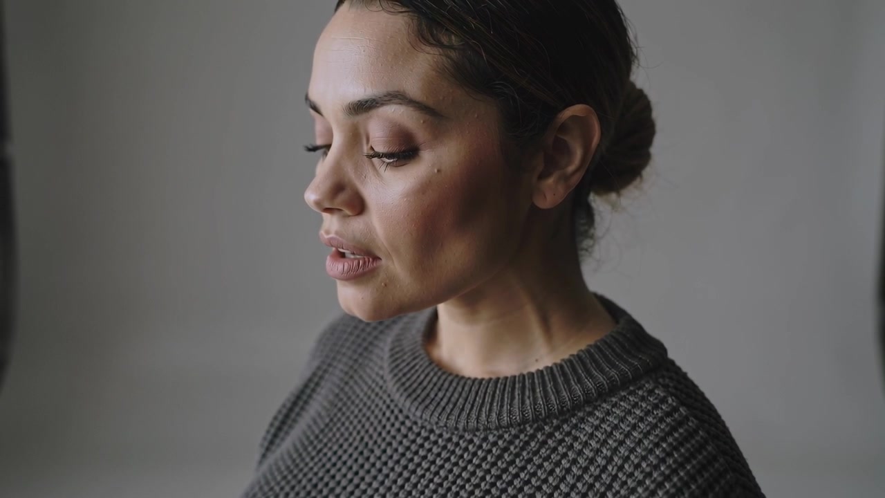 Pulling camera back model lowering chin and exhaling while showing charcoal knit sweater in studio