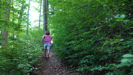 young man with red tshirt is running up a small path in the forest in slow motion