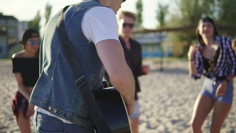 summer party on the beach. young friends drinking cocktails, dancing in the cirkle, playing guitar, singing songs and clapping on a beach at the water's edge. slowmotion shot