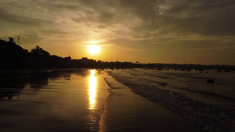 Aerial-flyover-calm-beach-shore,-early-morning-during-golden-paradise-sunrise