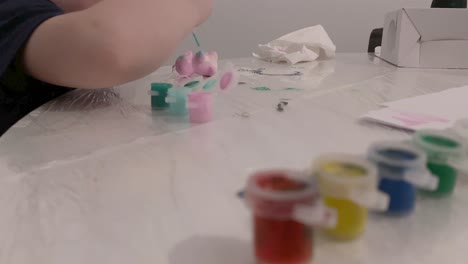 a child paints a small figure with paint. containers with paint in the foreground. close-up