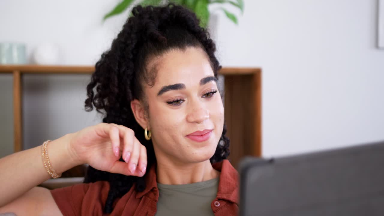 Afroameričanka přijímá online hovor na tabletu, sleduje obrazovku, usmívá se a kývá hlavou na pohovce.