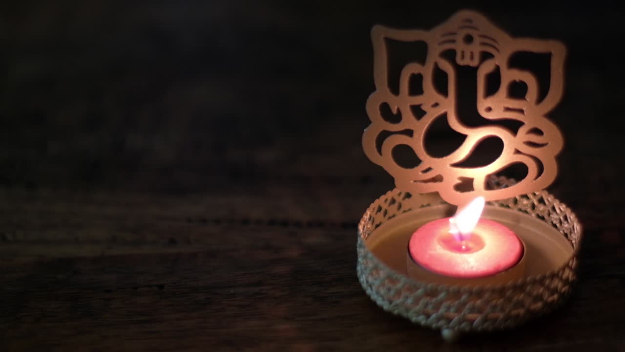 Primo piano con panoramica a destra su una sagoma di Ganesha con candela da tè, o Ganapati, Vinayaka, o con numerosi altri nomi, è una delle divinità più conosciute e venerate nel pantheon indù.