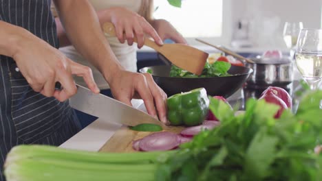 sección media de una pareja biracial cocinando juntos, cortando verduras en la cocina