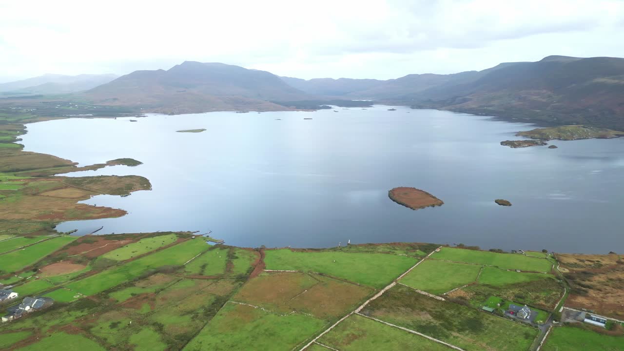 Drone footage of Lough Currane’s tranquil waters bordered by rolling fields and rugged hills around Waterville, County Kerry, captured in soft daylight across the Wild Atlantic Way