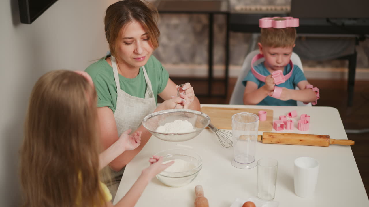 kid in yellow taps sieve to sift flour into bowl as baker holds handle with care, boy focused on toy shapes in background near piano, baking tools and eggs on kitchen table