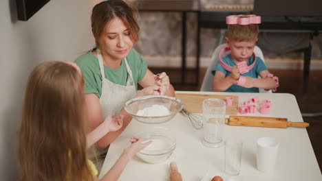 kid in yellow taps sieve to sift flour into bowl as baker holds handle with care, boy focused on toy shapes in background near piano, baking tools and eggs on kitchen table