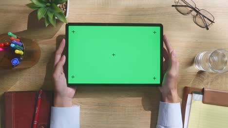 vista de arriba hacia abajo de una computadora portátil con pantalla verde simulada pantalla chromakey en un escritorio de oficina de madera al lado de la libreta con bolígrafos, gafas y un vaso de agua.