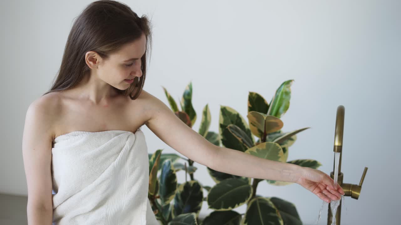 집 에서 목욕 을 하는 여자 가 손 으로 흐르는 물 을 만지는 온도 를 확인 하고 있다