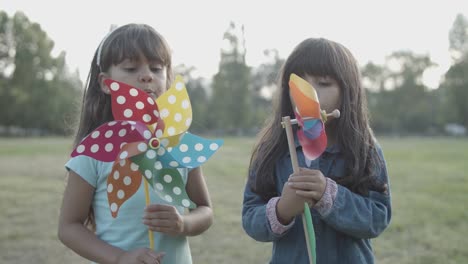 dos chicas latinas de pelo largo soplando abanicos de papel en el parque