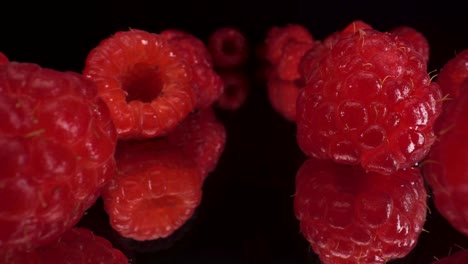 vista macro pasando por frambuesas rojas sobre fondo de vidrio negro reflectante, toma de 4k de fruta fresca saludable, dieta nutricional