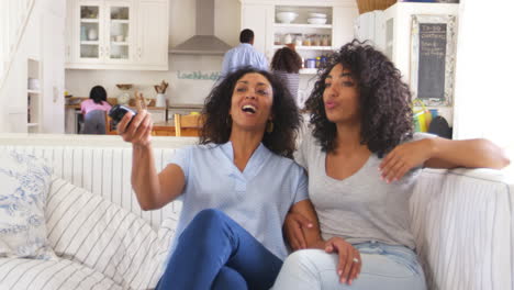 mother with teenage daughter sits on sofa watching tv together