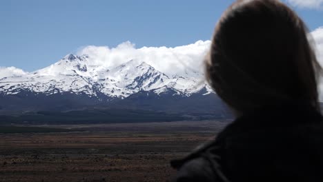 un monte ruapehu cubierto de nieve se cierne en la distancia mientras una turista mira la montaña