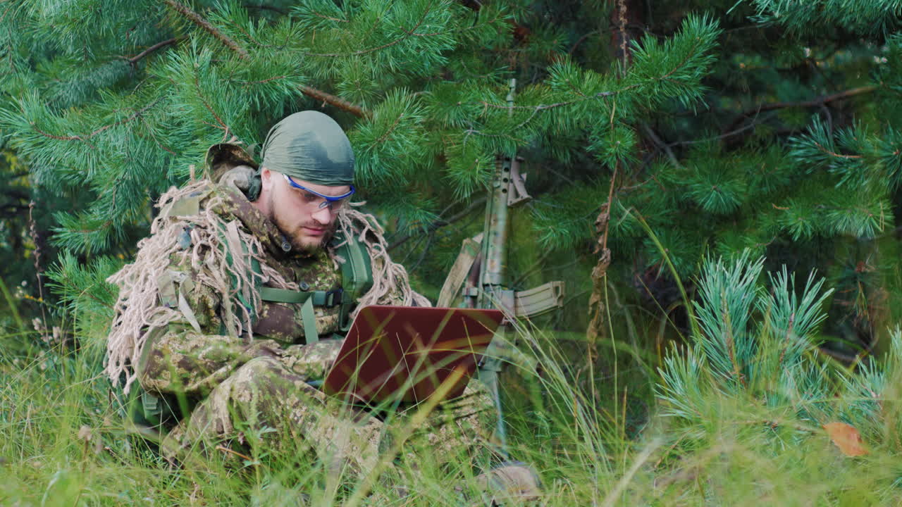 덤불 속에 앉아 있는 위장복을 입은 무장한 남자들은 노트북을 사용한다