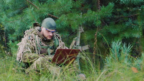 armed men in camouflage sitting in the bush uses a laptop