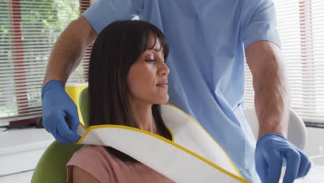 Caucasian-male-dentist-with-face-mask-preparing-smiling-female-patient-at-modern-dental-clinic