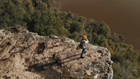 drone shot at the edge of a cliff from behind a woman takes pictures and looks at the landscape