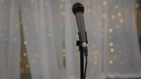 Wedding-Day-stock-clip-of-mic-microphone-on-stand-with-led-bokeh-lights-in-background-and-white-backdrop-ready-for-performer-singer-artist-or-toast-speeches