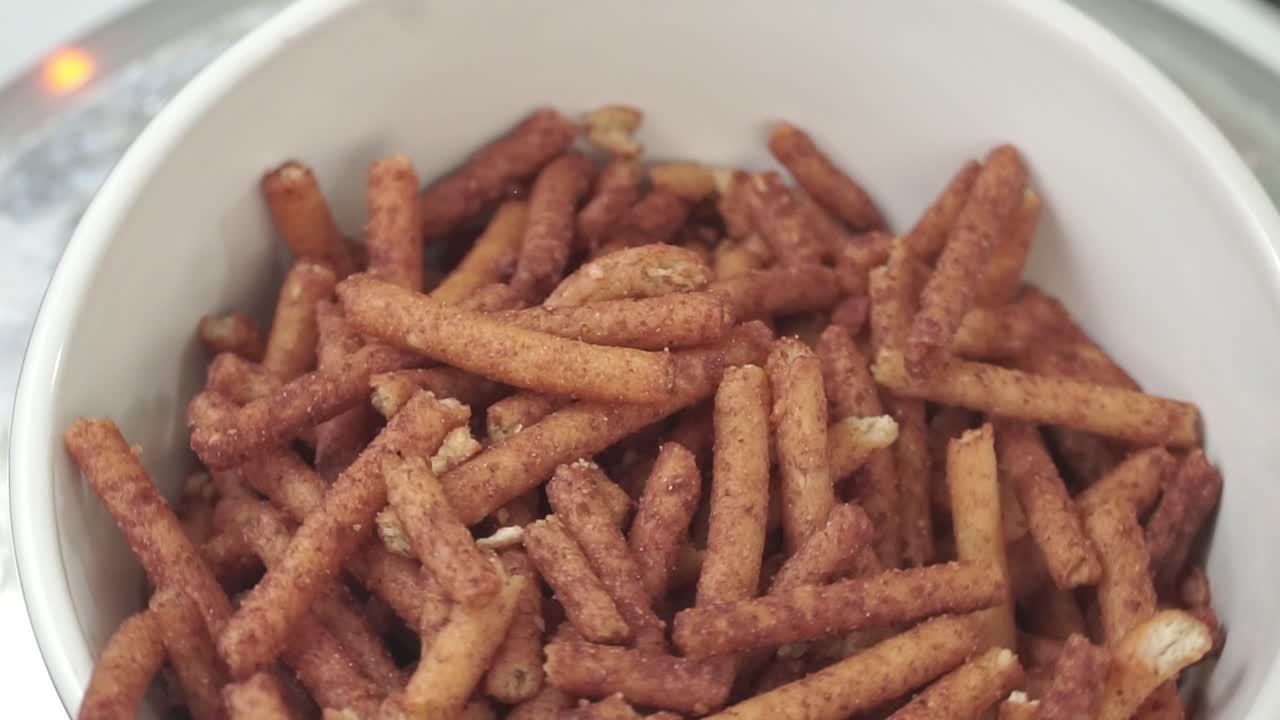 Close-up shot of salted snack sticks falling into rotating white bowl in soft light