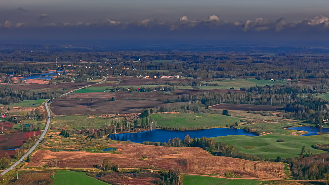 Farming landscape and a village, meadows, forests, and ponds below a flowing cloudscape high altitude time lapse - aerial view