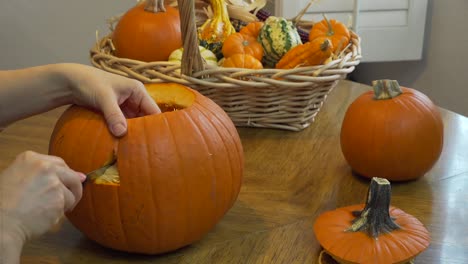 static shot of a woman cutting out the right eye of a pumpkin on a dining table with natural light from the side