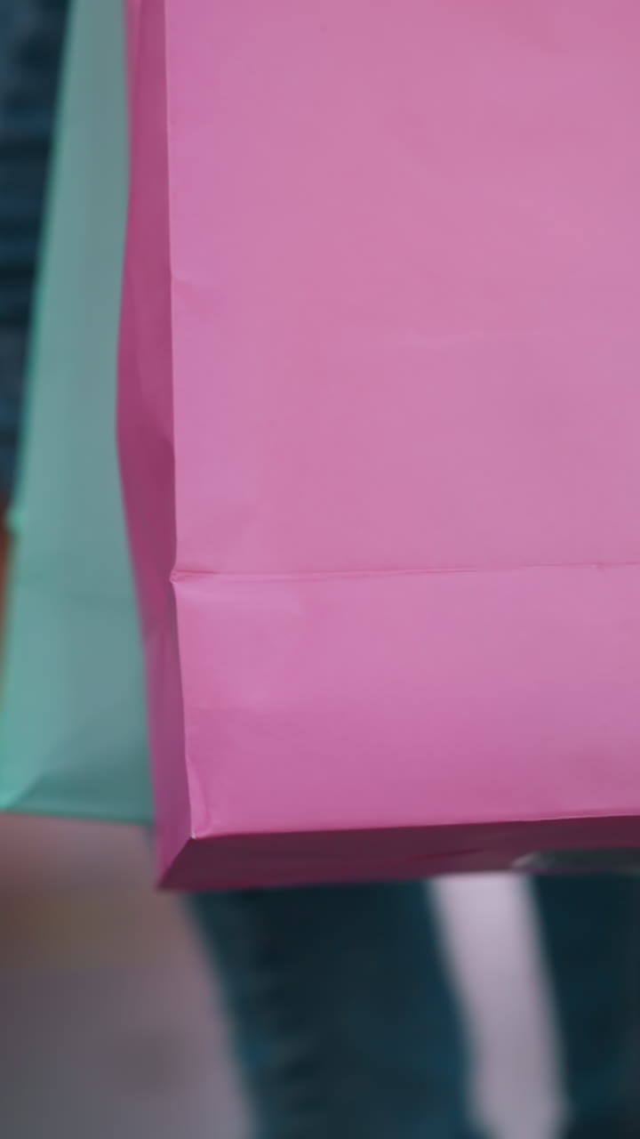 primer plano de una bolsa de compras rosada con una bolsa de menta ligeramente visible, llevada por un comprador que camina a través de un vibrante centro comercial, el fondo presenta una actividad bulliciosa