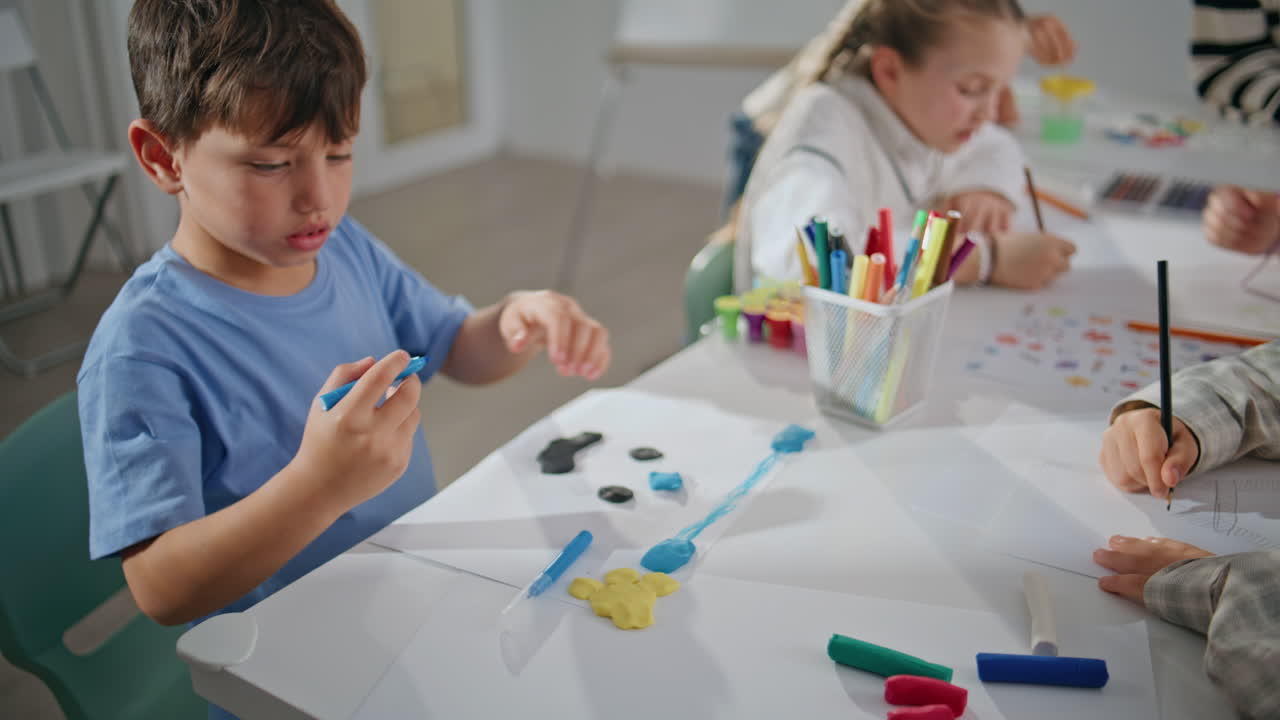 Little boy sculpting plasticine at school desk closeup. Pupil creating picture