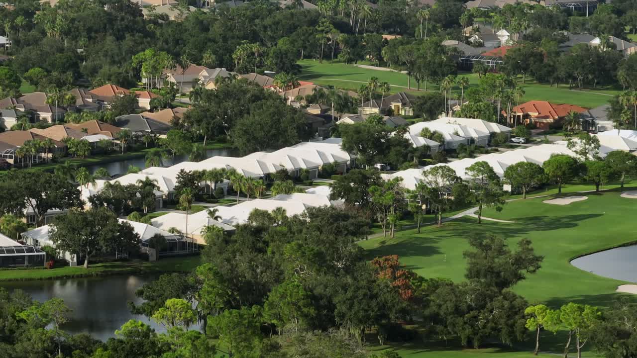 Noble American neighborhood with homes and houses between palm trees. Sunset time in Florida, USA. Aerial zoom shot. Golf course in Florida sunshine state