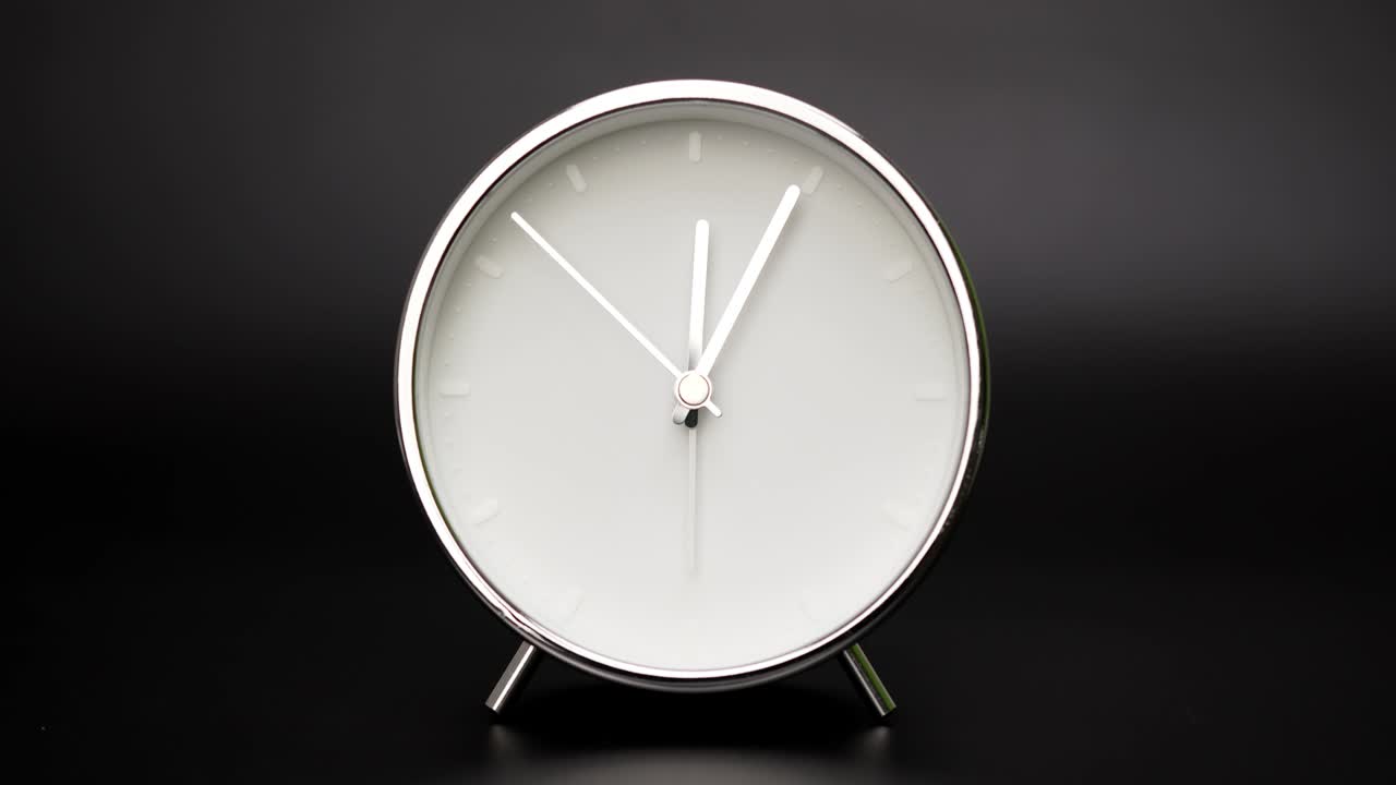 Twelve o'clock Silver Alarm clock on black background.