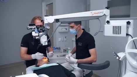 male dentist with his assistant treat patient's teeth. modern technologies in dentistry. stomatologist examines woman's mouth through the microscope.