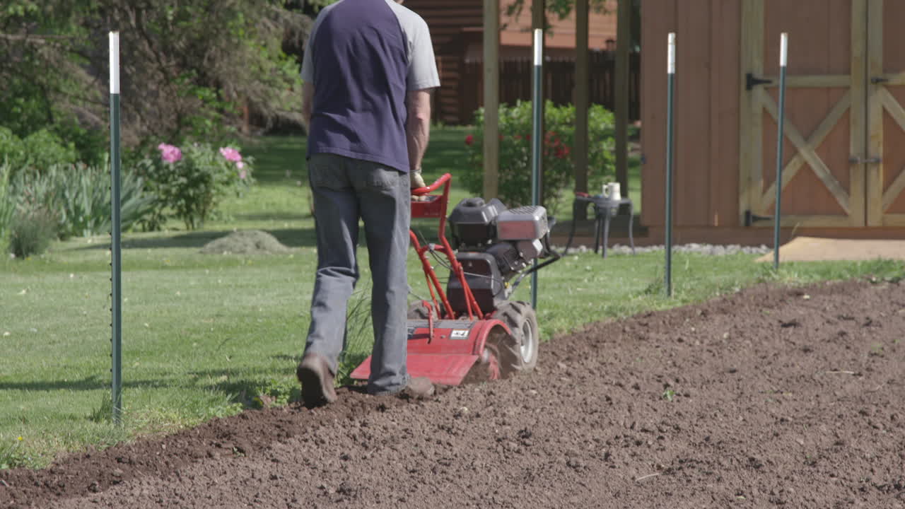 un hombre prepara su jardín usando un motocultor para el suelo