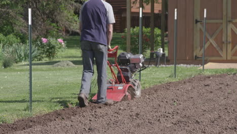 a man prepares his garden by using a rototiller for the soil