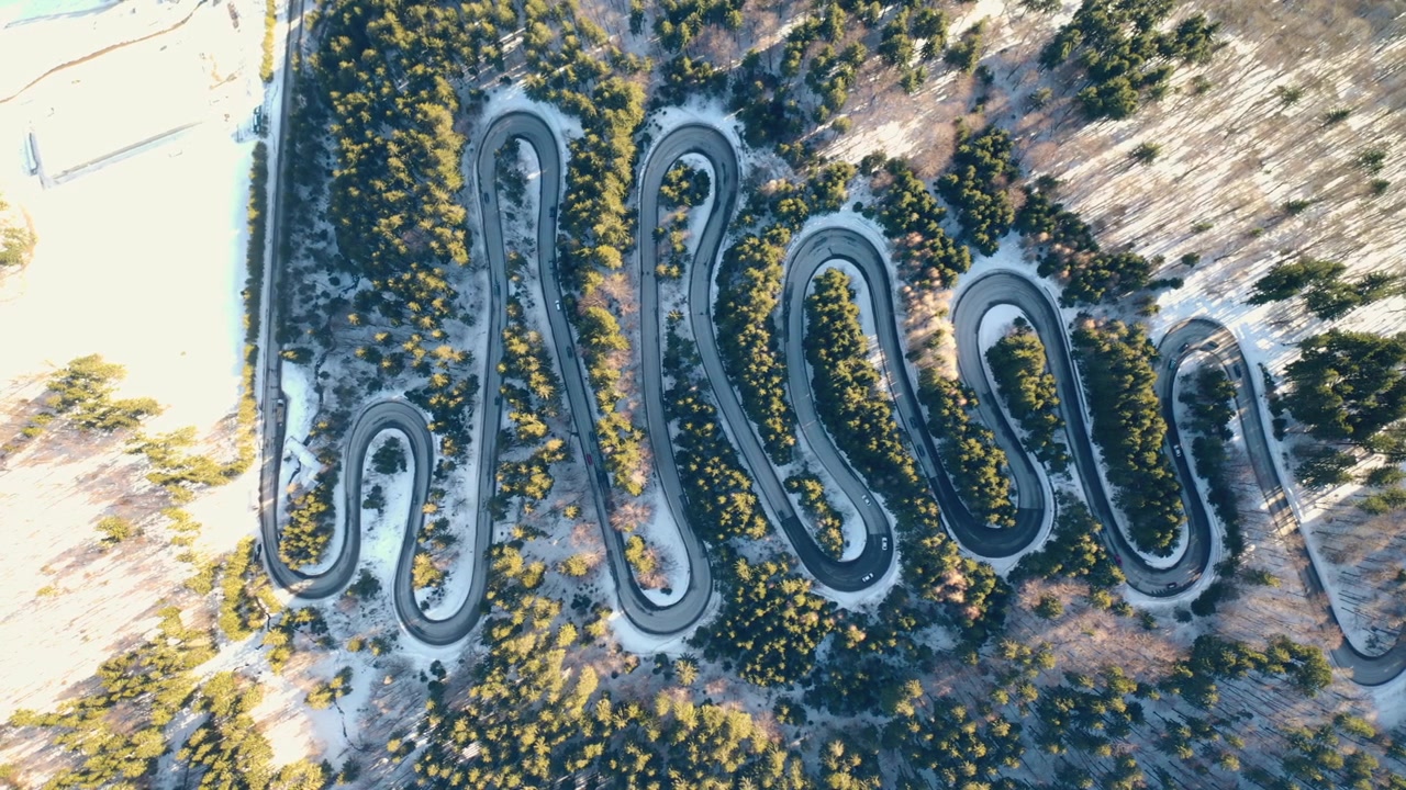 4k luftfoto ovenfra av motorsykler og biler som kjører på en veldig svingete vei. Svingete serpentinvei med hårnålssvinger som snor seg gjennom skogen i Transylvania, Europa