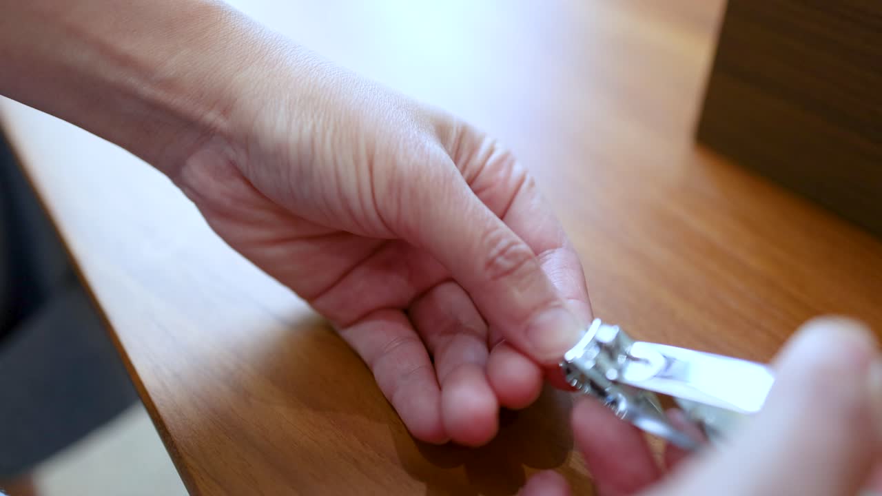 Un primo piano di una mano asiatica che si taglia le unghie con un tagliaunghie di metallo, al chiuso