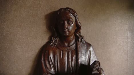 estatua de madera de jesucristo sosteniendo la biblia detrás de una planta en un hogar religioso