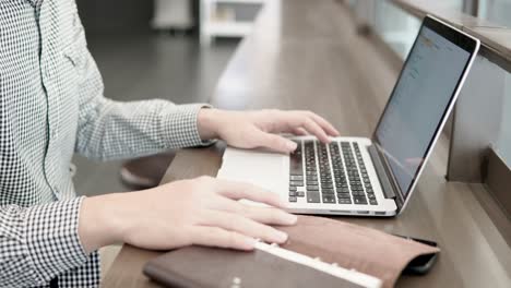 young university student man using laptop computer in working space. male hand opening notebook on wooden desk for checking information. college lifestyle or educational research concepts.