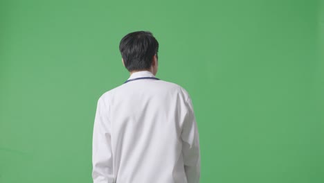 back view of asian male doctor with stethoscope waving hand and smiling while walking on green screen background in the hospital