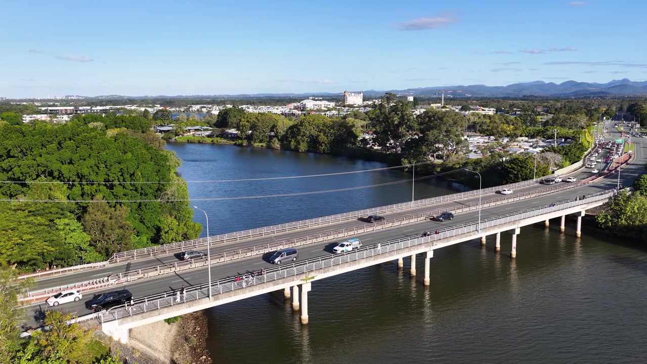 Ripresa aerea con drone dall'alto di auto che attraversano un ponte fluviale sotto un cielo azzurro e limpido