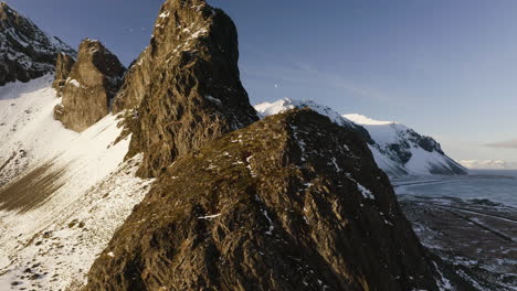 aerial view backwards from bird covered, rocky peaks, sunlit by the winter sun of iceland - pull back, drone shot