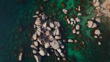 lake tahoe birdseye view shoreline large boulder rocks crystal clear glassy turquoise fresh water aerial drone sand harbor california sunny daytime winter secret chimney beach upwards motion