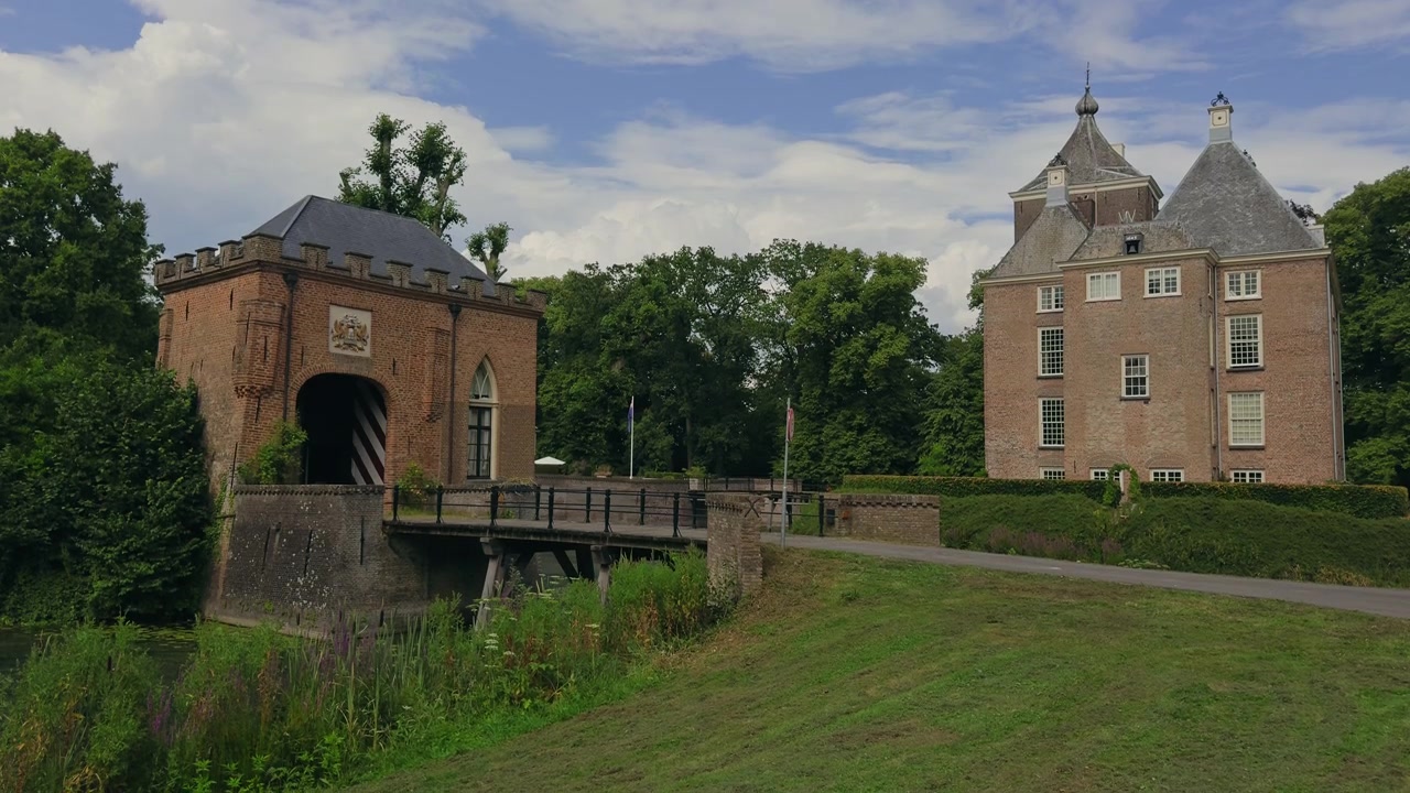 Veduta statica del Castello di Neerijnen e del suo ponte d'ingresso sul fossato circostante, incorniciato dal verde sotto un cielo estivo azzurro con soffici nuvole di cotone