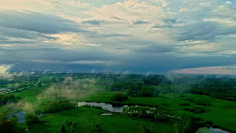 green rural landscape with stormy clouds above, aerial drone view