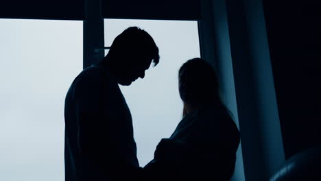 silhouettes of expecting couple standing at the window. man strokes big wife's belly and then embraces her. low angle view.