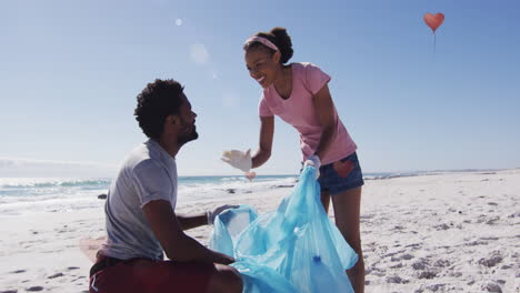 animación de iconos del globo sobre un feliz hombre y mujer afroamericanos recogiendo basura de la playa